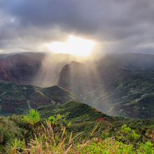 The sun bursts through the clouds over a mountainous landscape